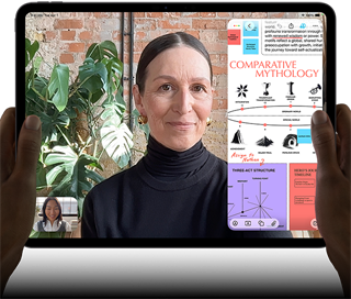 iPad Pro i space black vist forfra i vandret position, afrundede hjørner, sort skærmkant, et par hænder holder enheden på venstre og højre side, skærmen viser et FaceTime-opkald, der oversættes live, en uddannelsesapp viser en præsentation af “Comparative Mythology” med tekst, diagrammer og håndskrevne noter